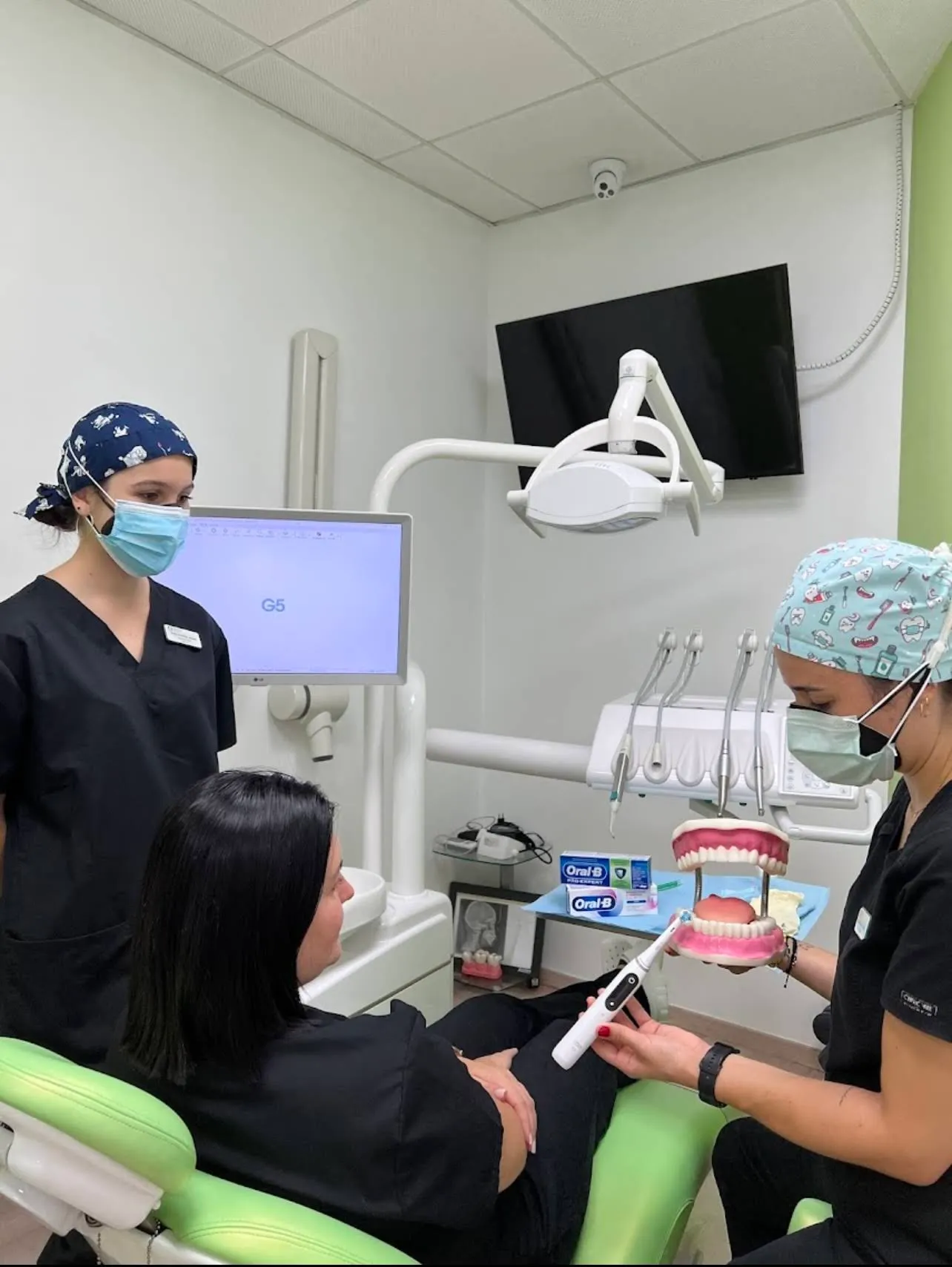 Dos profesionales de la clínica enseñando la técnica de cepillado a una paciente en el gabinete dental